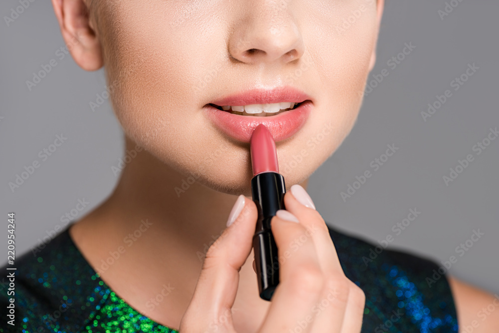 partial view of woman applying lipstick isolated on grey