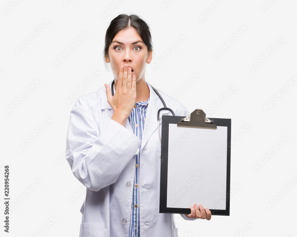 Young hispanic doctor woman holding clipboard cover mouth with hand shocked with shame for mistake, expression of fear, scared in silence, secret concept Young hispanic doctor woman holding clipboard cover mouth with hand shocked with shame for mistake, expression of fear, scared in silence, secret concept