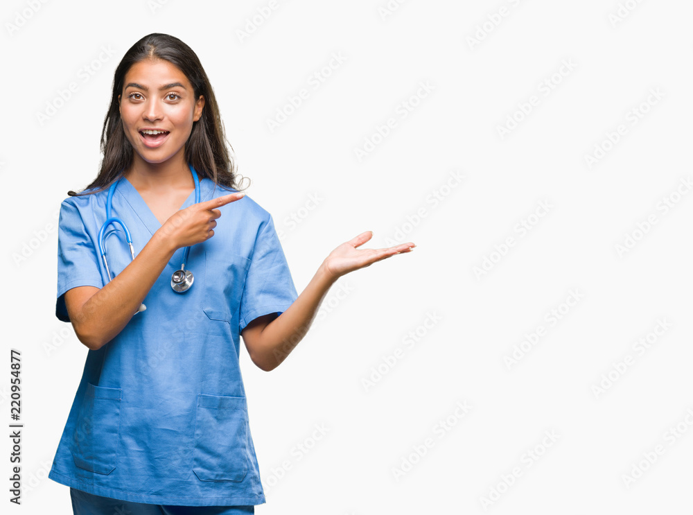Young arab doctor surgeon woman over isolated background amazed and smiling to the camera while presenting with hand and pointing with finger. Young arab doctor surgeon woman over isolated background amazed and smiling to the camera while presenting with hand and pointing with finger.