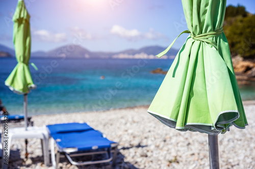 Green sunbed umbrella on white stoe beach by clear turquoise blue waters of Mediterranean sea on sunny hot summer day photo
