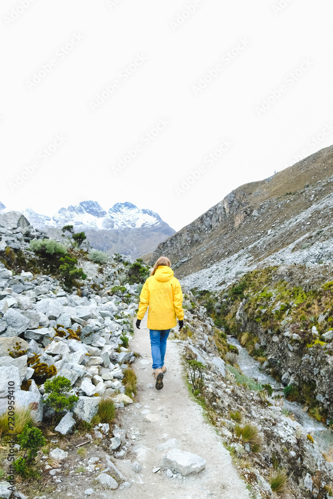The girl walks along the path in a yellow jacket. Around the snow mountains. Peru The girl walks along the path in a yellow jacket. Around the snow mountains. Peru