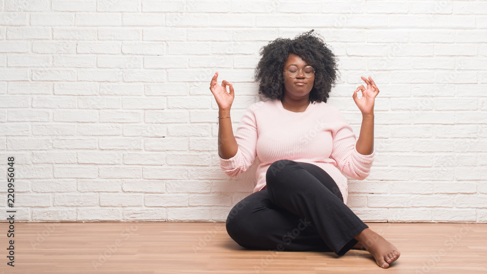 Young african american woman sitting on the floor at home relax and smiling with eyes closed doing meditation gesture with fingers. Yoga concept. Young african american woman sitting on the floor at home relax and smiling with eyes closed doing meditation gesture with fingers. Yoga concept.