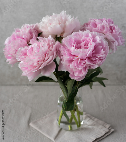 a bouquet of blossomed pink peonies in a vase, grey background