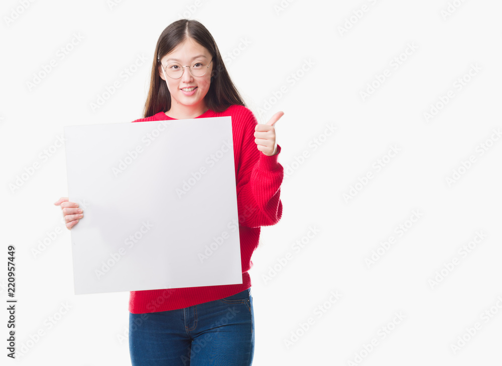 Young Chinese woman over isolated background holding blank banner happy with big smile doing ok sign, thumb up with fingers, excellent sign Young Chinese woman over isolated background holding blank banner happy with big smile doing ok sign, thumb up with fingers, excellent sign
