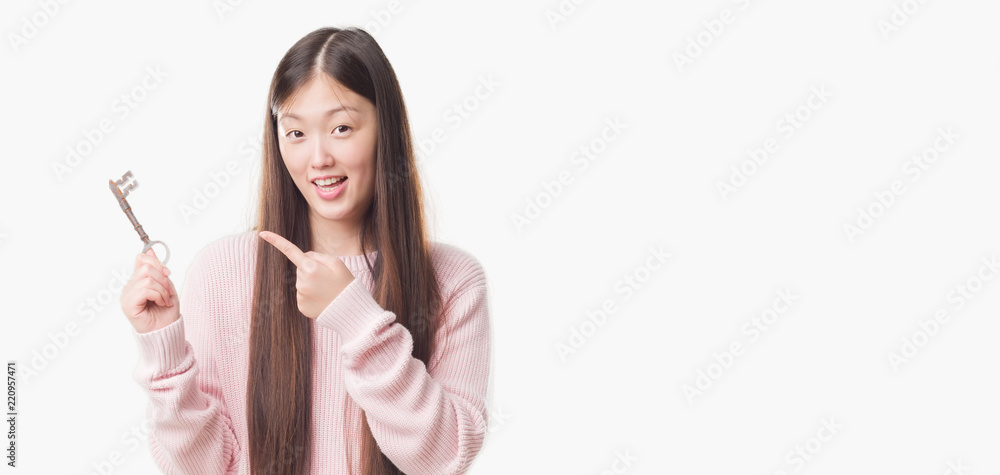 Young Chinese real state agent woman over isolated background holding vintage key very happy pointing with hand and finger Young Chinese real state agent woman over isolated background holding vintage key very happy pointing with hand and finger