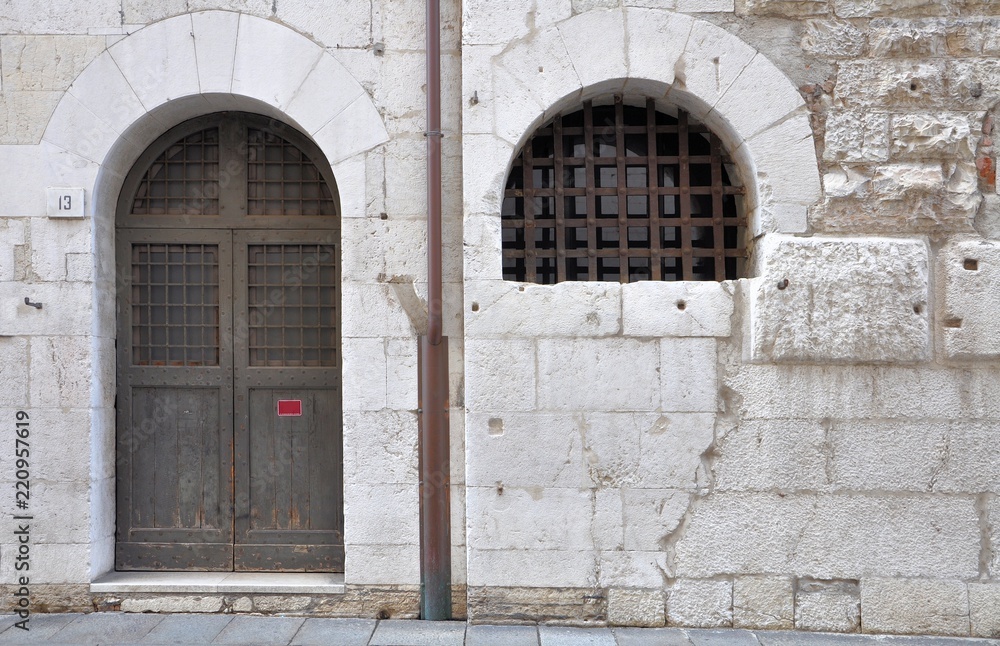 Fototapeta premium Gothic window and arched door with iron grating in ancient stone wall.