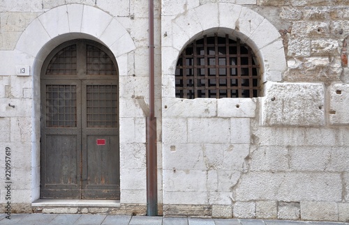 Gothic window and arched door with iron grating in ancient stone wall.
