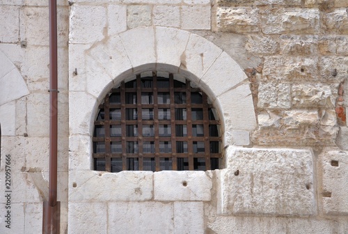 Gothic arched window with iron grating in an ancient stone wall.