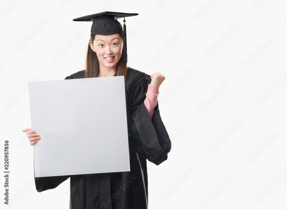 Young Chinese woman wearing graduate uniform holding banner screaming proud and celebrating victory and success very excited, cheering emotion Young Chinese woman wearing graduate uniform holding banner screaming proud and celebrating victory and success very excited, cheering emotion
