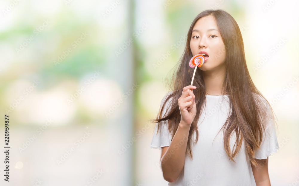 Young asian woman eating lollipop candy over isolated background with a confident expression on smart face thinking serious