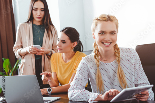 smiling businesswoman with digital tablet and her colleagues behind at modern office