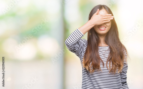 Young asian woman wearing glasses over isolated background smiling and laughing with hand on face covering eyes for surprise. Blind concept.
