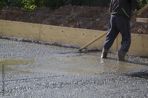 worker in rubber boots stands in uncluttered cement and leveling the surface of the base plate (fresh concrete slab) with a special wooden working tool