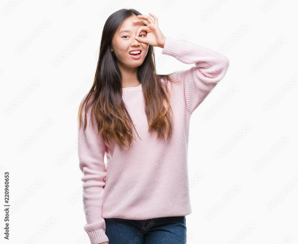 Young asian woman over isolated background doing ok gesture with hand smiling, eye looking through fingers with happy face. Young asian woman over isolated background doing ok gesture with hand smiling, eye looking through fingers with happy face.