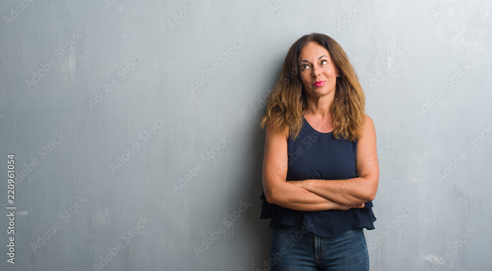 Middle age hispanic woman standing over grey grunge wall smiling looking side and staring away thinking. Middle age hispanic woman standing over grey grunge wall smiling looking side and staring away thinking.