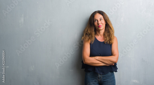 Middle age hispanic woman standing over grey grunge wall smiling looking side and staring away thinking.
