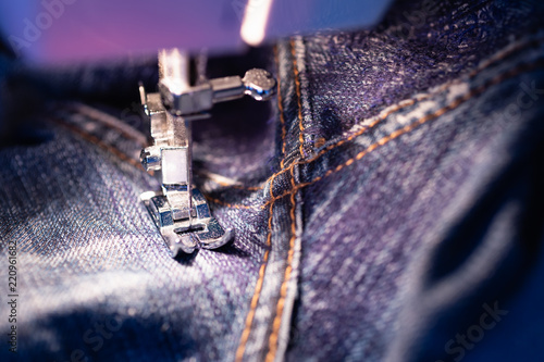 Repair jeans on the sewing machine. View of the fabric, needle and thread. Illumination from the built-in incandescent lamp. Jeans are a type of trousers, typically made from denim or dungaree cloth.