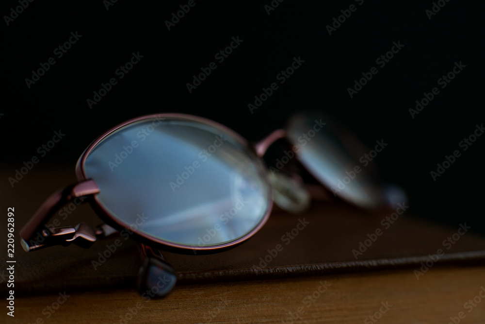 Glasses on a closed book. Macro. Glasses and book on a black background. Glasses close-up on a blurred background. Glasses on a closed book. Macro. Glasses and book on a black background. Glasses close-up on a blurred background.