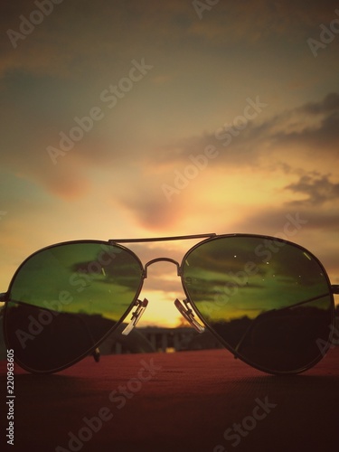 Sunglasses on the table with sunset background.