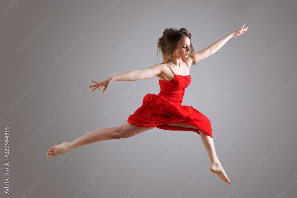 elegant female dancer in red dress jumping against gray background