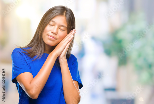 Young asian woman over isolated background sleeping tired dreaming and posing with hands together while smiling with closed eyes. Free Download Young asian woman over isolated background sleeping tired dreaming and posing with hands together while smiling with closed eyes. - GFXLoad