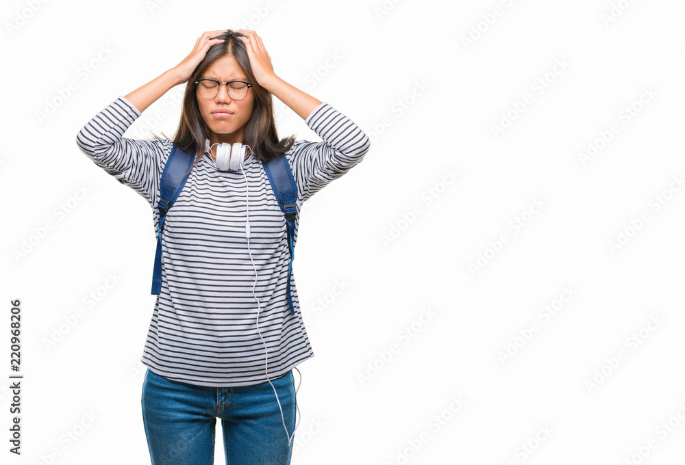 Young asian student woman wearing headphones and backpack over isolated background suffering from headache desperate and stressed because pain and migraine. Hands on head. Young asian student woman wearing headphones and backpack over isolated background suffering from headache desperate and stressed because pain and migraine. Hands on head.
