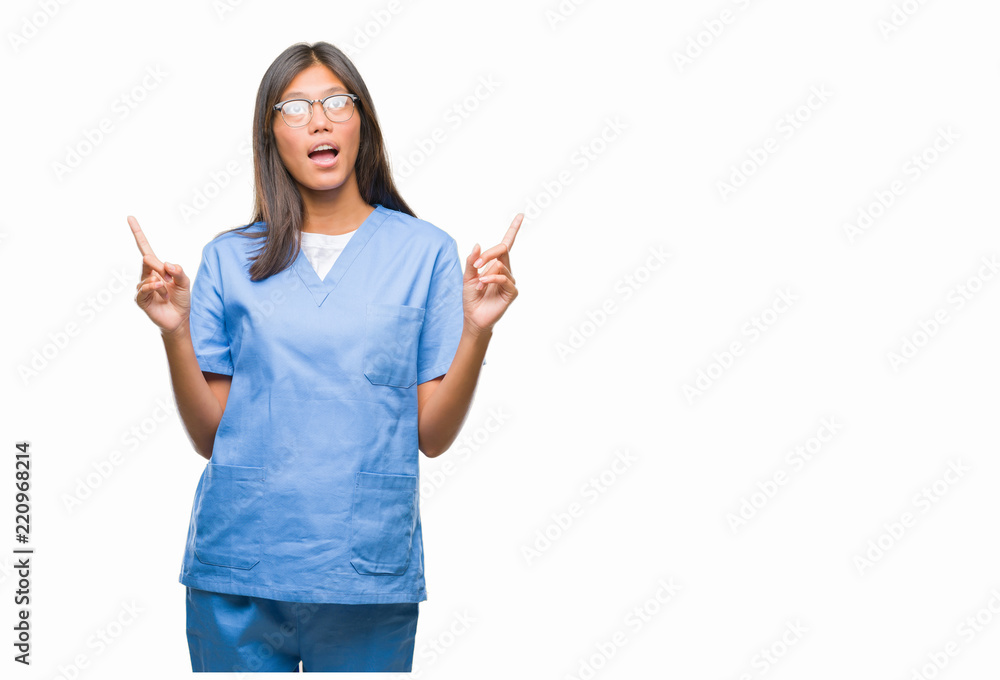 Young asian doctor woman over isolated background amazed and surprised looking up and pointing with fingers and raised arms. Young asian doctor woman over isolated background amazed and surprised looking up and pointing with fingers and raised arms.