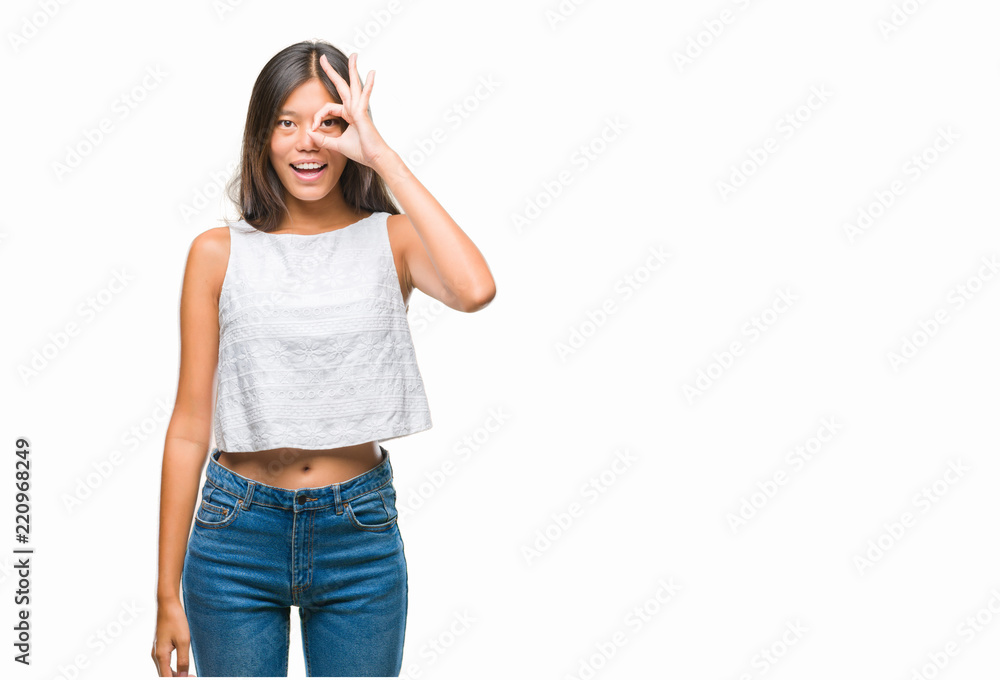 Young asian woman over isolated background doing ok gesture with hand smiling, eye looking through fingers with happy face. Young asian woman over isolated background doing ok gesture with hand smiling, eye looking through fingers with happy face.