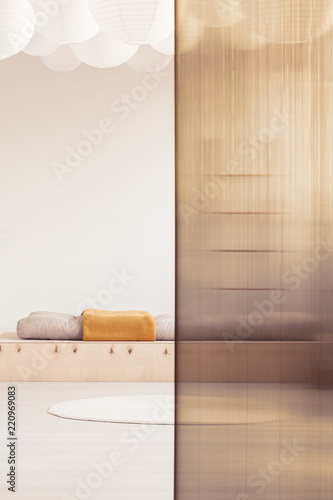 Orange blanket on wooden bed in minimal bedroom interior with rug and screen. Real photo photo