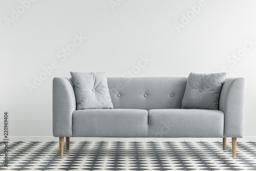 Grey sofa with pillows on patterned floor in minimal living room interior. Real photo