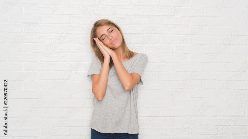 Beautiful young woman over white brick wall sleeping tired dreaming and posing with hands together while smiling with closed eyes. Beautiful young woman over white brick wall sleeping tired dreaming and posing with hands together while smiling with closed eyes.