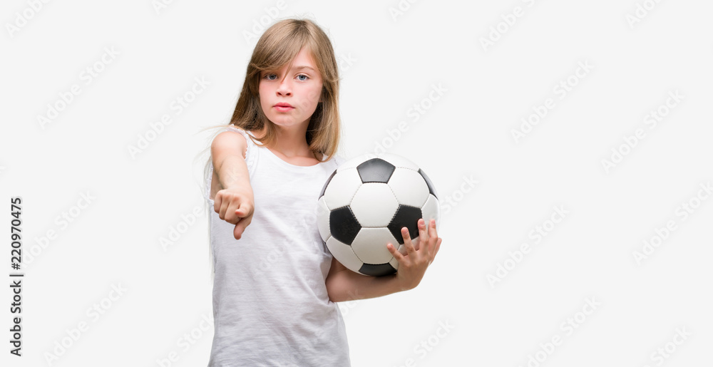 Young blonde toddler holding football ball pointing with finger to the camera and to you, hand sign, positive and confident gesture from the front