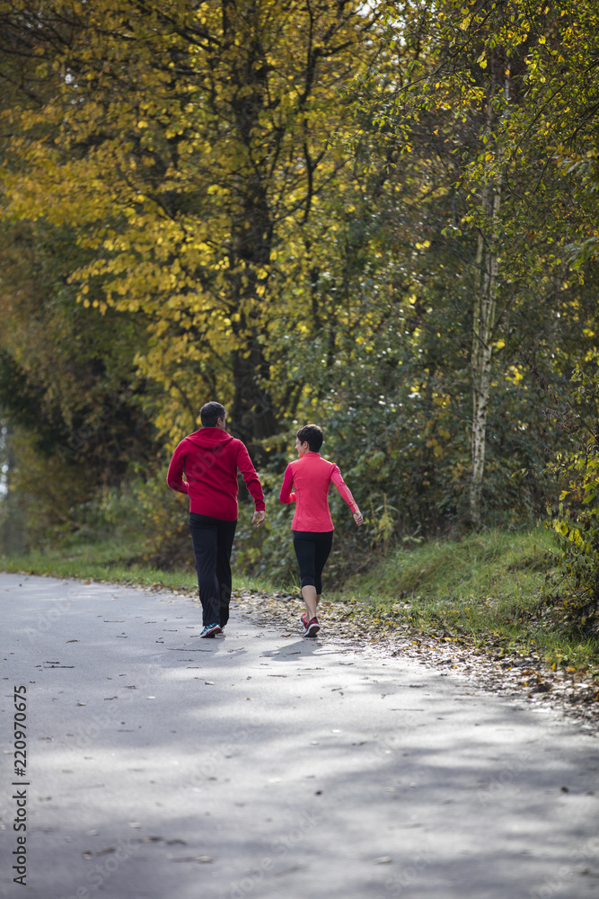 Fototapeta premium Young couple running on the sunny day in the autumn forest of the Bavarian National Park, Bavaria, Germany