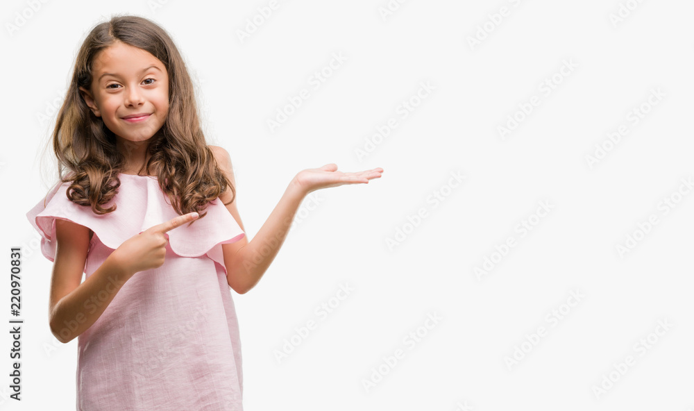 Brunette hispanic girl wearing pink dress amazed and smiling to the camera while presenting with hand and pointing with finger. Brunette hispanic girl wearing pink dress amazed and smiling to the camera while presenting with hand and pointing with finger.