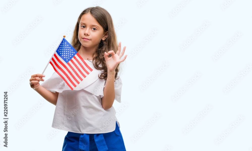 Brunette hispanic girl holding flag of United States of America doing ok sign with fingers, excellent symbol Brunette hispanic girl holding flag of United States of America doing ok sign with fingers, excellent symbol