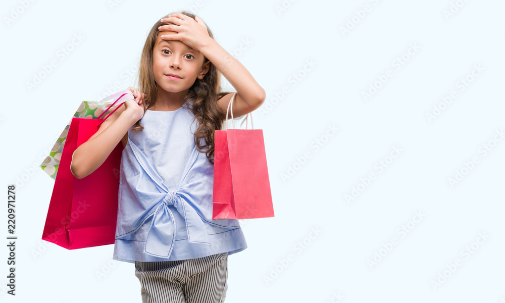 Brunette hispanic girl holding shopping bags stressed with hand on head, shocked with shame and surprise face, angry and frustrated. Fear and upset for mistake.