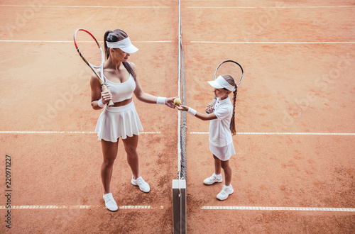 confident tennis coach and little girl standing against against each other before the game. © HBS