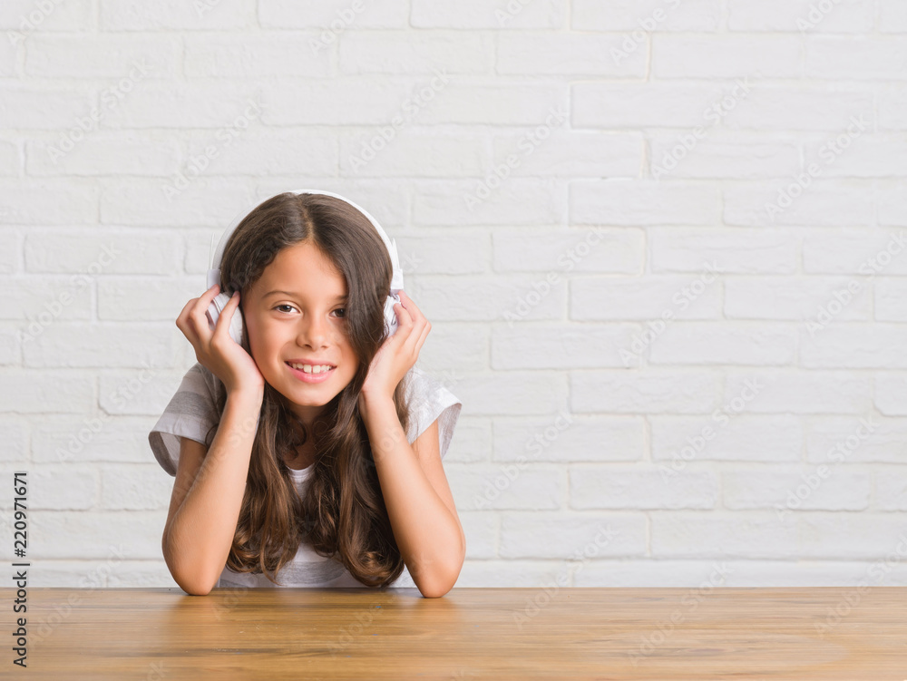 Young hispanic kid sitting on the table wearing headphones with a happy face standing and smiling with a confident smile showing teeth Young hispanic kid sitting on the table wearing headphones with a happy face standing and smiling with a confident smile showing teeth
