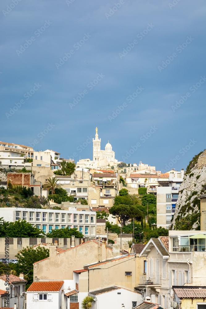 The immaculate basilica of Notre-Dame de la Garde in Marseille, France, on top of the hill seen from the Vallon des Auffes by a stormy summer day against a dark cloudy sky.