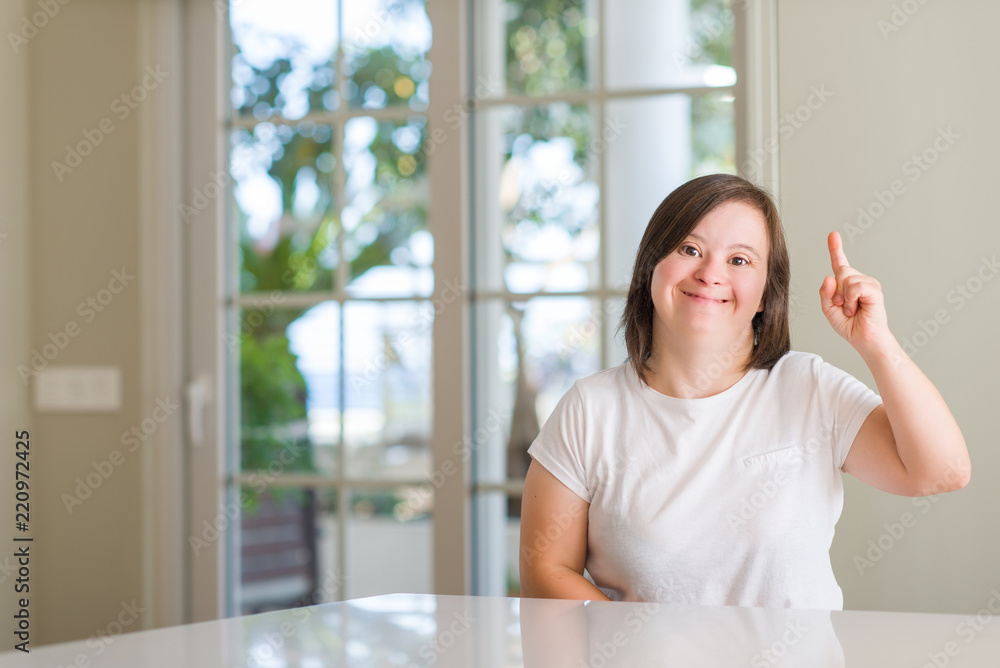 Down syndrome woman at home pointing finger up with successful idea. Exited and happy. Number one. Down syndrome woman at home pointing finger up with successful idea. Exited and happy. Number one.