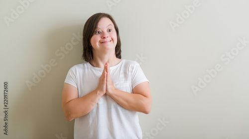 Photography Down syndrome woman standing over wall begging and praying with hands together with hope expression on face very emotional and worried