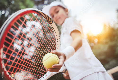 Sporty little girl preparing to serve tennis ball. Close up of beautiful yong girl holding tennis ball and racket. Child tennis player preparing to serve.