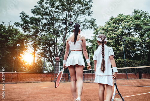 That was a great game! Cropped rear view of two sporty female athlete on tennis court. Girl and her tennis instructor going to the tennis court. Family leisure. © HBS