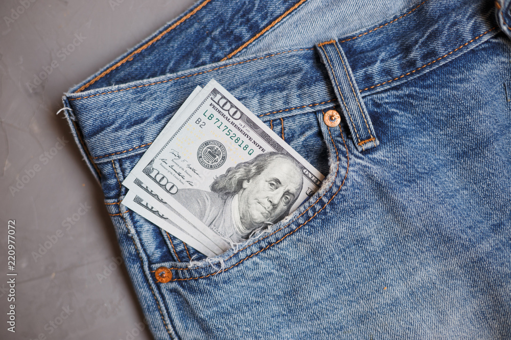 Moscow, Russia - 08 30 2018: Money financial concept. Dollar banknotes in a pocket of blue jeans on gray background. Moscow, Russia - 08 30 2018: Money financial concept. Dollar banknotes in a pocket of blue jeans on gray background.