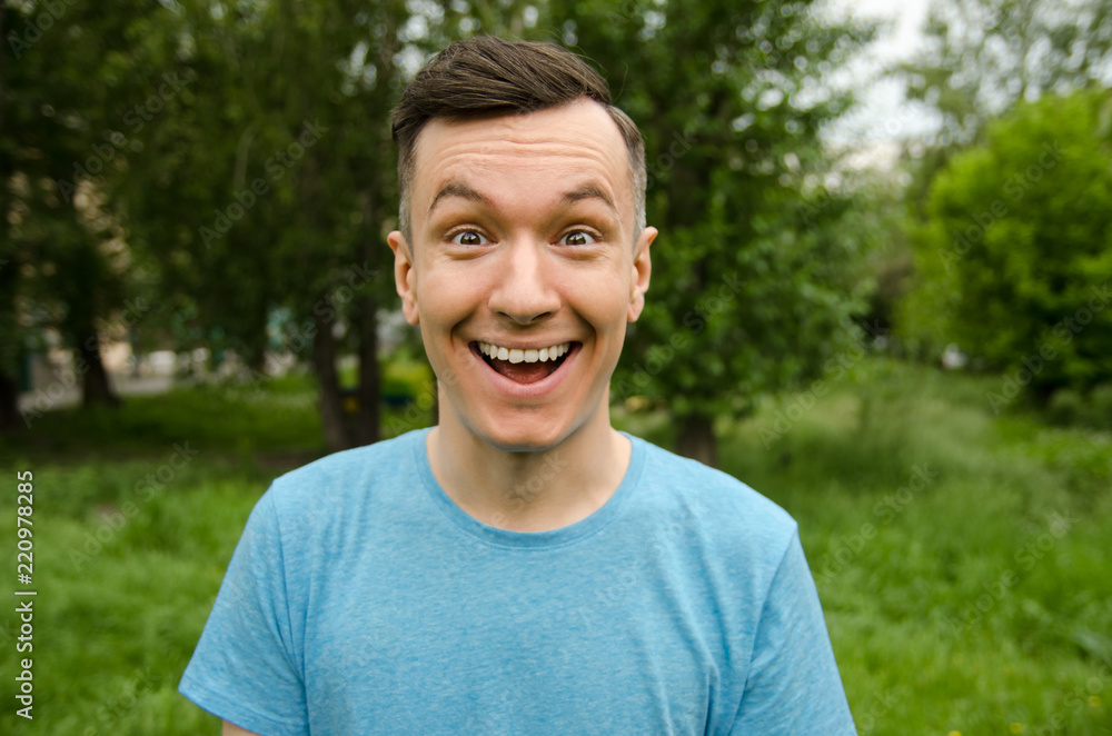 Young smiling joyful guy on a green grass and trees background. Young smiling joyful guy on a green grass and trees background.