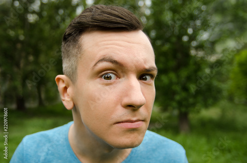 Foto Young guy with a questioning gaze on a green grass and trees background