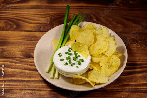 Crispy potato chips with green onion and sour cream on wooden table