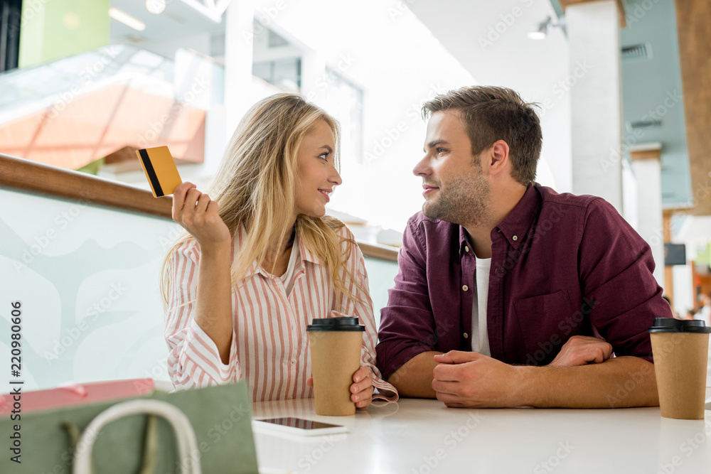 couple with credit card and disposable cups of coffee looking at each other at table in cafe couple with credit card and disposable cups of coffee looking at each other at table in cafe