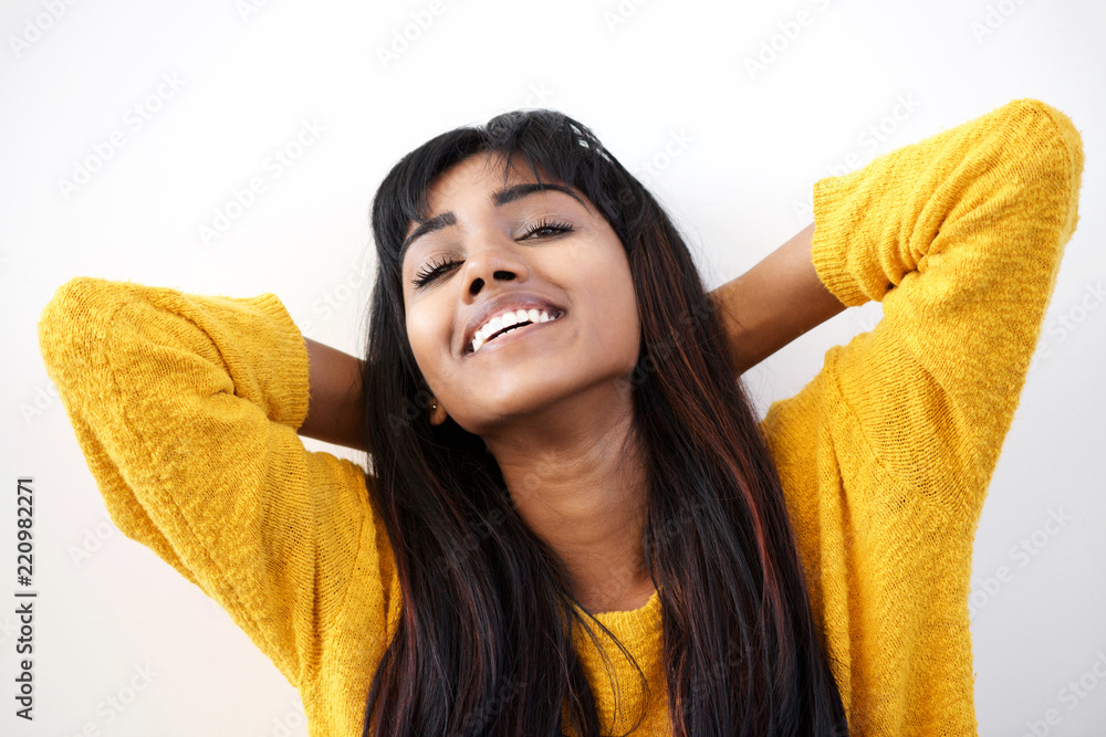 Close up smiling young Indian woman with hands behind head against white background Close up smiling young Indian woman with hands behind head against white background