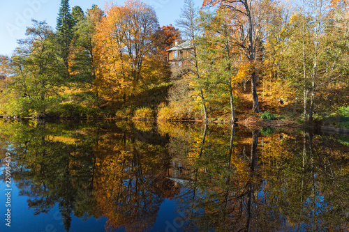 Trees in autumn colors on a lake with a house on a hill reflected in water